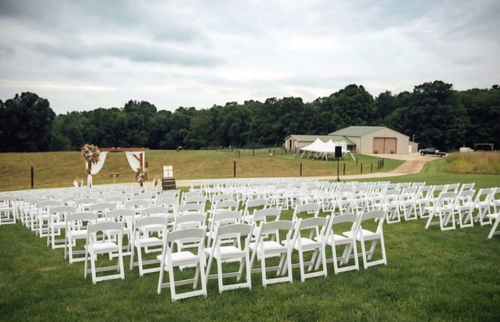 Rows of white folding wedding chairs arranged on grass for an outdoor wedding ceremony.